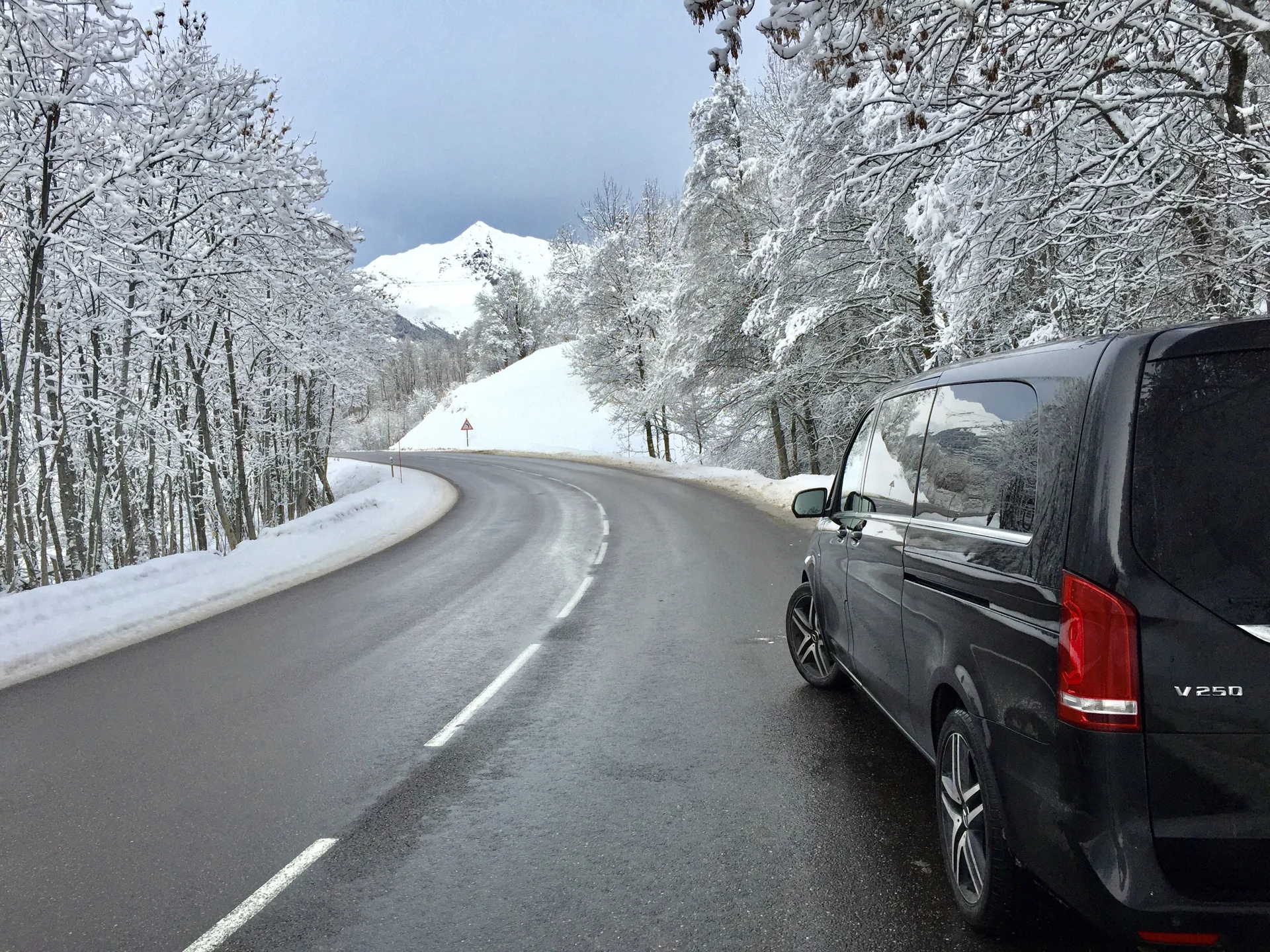 Mercedes V-Class on an Alpine road lined with snow-covered trees.
