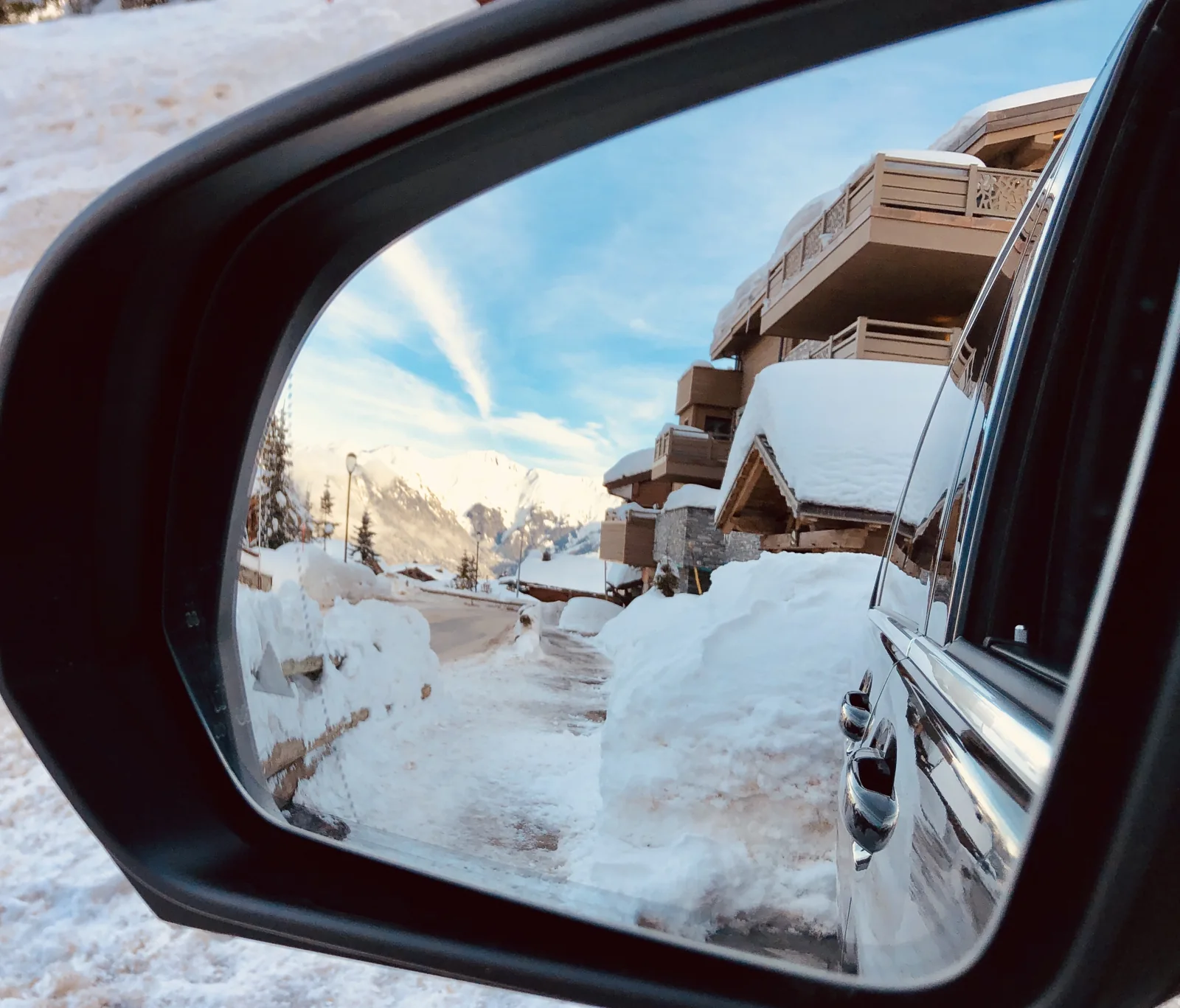Un chalet et la neige se reflètent dans le rétroviseur du van.