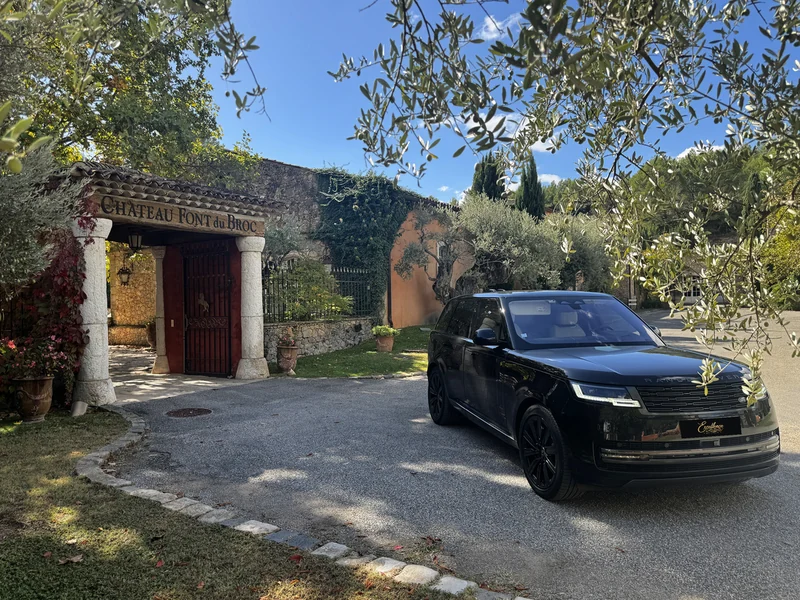 Black Range Rover at the stone entrance to Château Font du Broc beneath olive branches, with a black Excellence presentation plate.